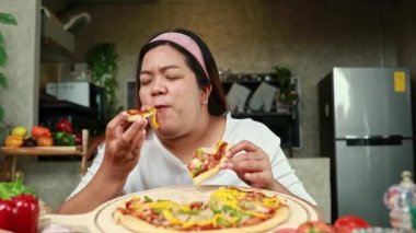 Fat asian happy woman sits and eats her favorite food pizza with great relish greedily overeating causes choking.