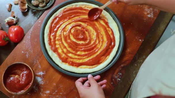 自家製ピザを作る女性シェフキッチン表面においしい赤いトマトソースを塗っマリネ生地は オーブンに入る前にピザのトッピングとチーズを準備します — ストック動画