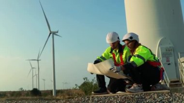 Teamwork two caucasian technicians inspect stands analyzing wind power station area blueprints, generating energy with wind turbines as a clean and environmentally friendly energy force.