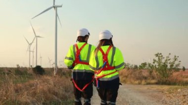 Teamwork two caucasian technicians inspect stands analyzing wind power station area blueprints, generating energy with wind turbines as a clean and environmentally friendly energy force.