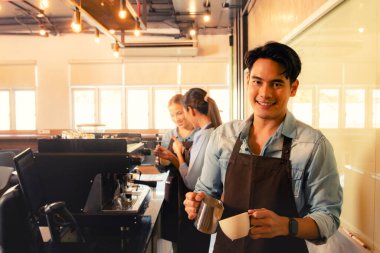 Portre yakışıklı Asyalı barista sütlü köpüğü sütlü kahve bardağına döker. Kahve fincanının içine güzel bir iştah açıcı bir tat katar. Kahve kafeteryasında müşterilere servis yapan güzel barista personeliyle birlikte..