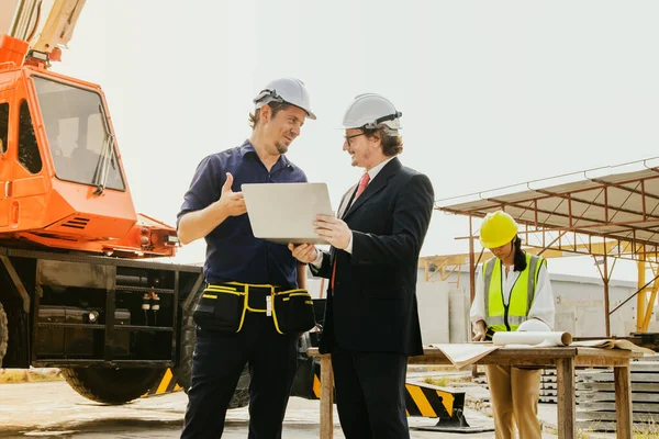 Male business partners and technicians, owners of prefabricated house walls, consulting in the field work, discussing joint ventures in construction business together in the construction area.