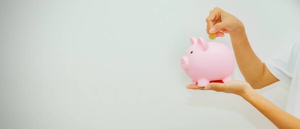 Banner side view : Young woman's hand holding piggy bank and gold coin to promote future savings. business, Investment, retirement, insurance. education : Saving money concept.