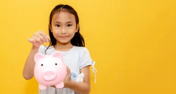 Portrait young girls asian elementary school students enjoy happy saving money use coins to put pink pig piggy bank Collect coins with pride : Saving allowance money for education concept : Copy space