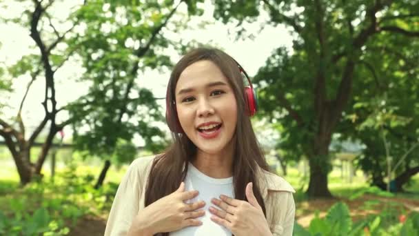良い気分でヘッドフォンを持つアジアの女子大生は素晴らしい森林環境について説明しています — ストック動画