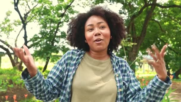 明るい顔と良い自然笑顔の若いアフリカ系アメリカ人女性の肖像画が立っており 緑豊かな庭の環境を説明します 自分自身を楽しませ 良い精神にある — ストック動画