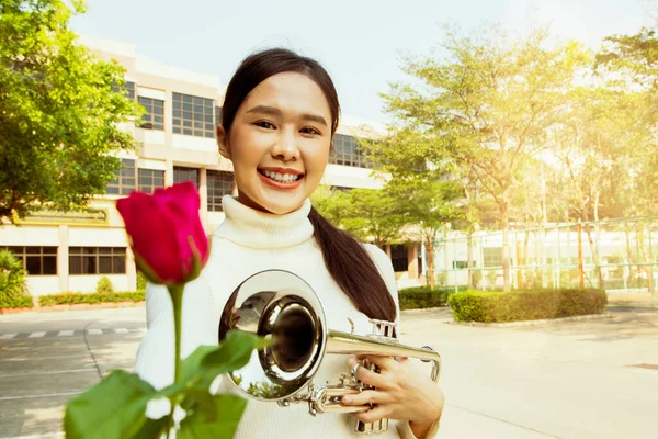 International music teacher in school : Portrait beautiful asian teacher healthy holding bright red rose and trumpet in front of school building handing flowers with friendly smile to lovely student.