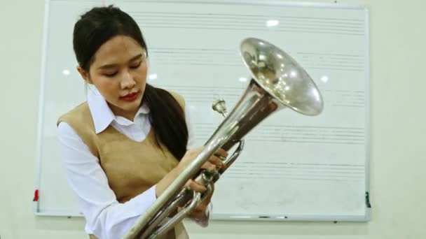 バリトン楽器に興味を持つアジア系女性の学生が練習しているが 彼女はそれを使用する方法を混乱させるノートを爆破し 押す方法がわからない — ストック動画