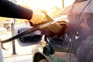 EV elektrikli araba kullanan genç bir kadın, benzin istasyonundaki gri ve siyah elektrikli akü prizine takılıyor: Temiz enerji aracı Alternatif enerji popüler bir kavram haline geliyor.