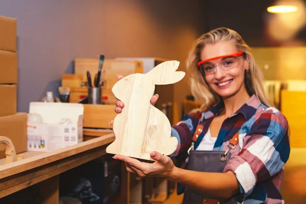 Cacausian female carpenter smiles admiring the masterpieces of wooden rabbit-shaped furniture for beautifying home decor : The beautiful woodwork designers show off their work in admiration.