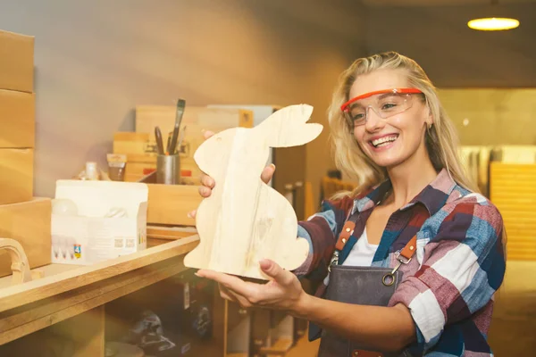 Cacausian female carpenter smiles admiring the masterpieces of wooden rabbit-shaped furniture for beautifying home decor : The beautiful woodwork designers show off their work in admiration.