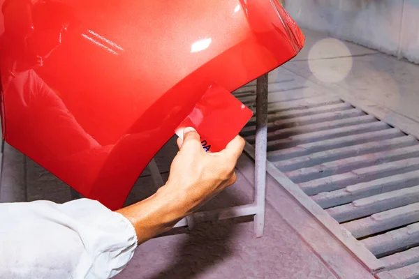 Hand of a male auto painter working car painting room inspects and compares the red paint to the sheet metal sprayed front bumper to get similar and beautiful color : Jobs in auto repair garages.