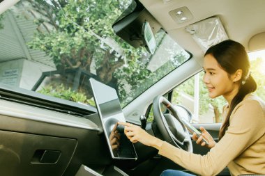 EV elektrikli araç kullanan Asyalı genç bir kadın kabinde oturmuş modern dokunmatik ekran düzeneğini inceliyor. İyi bir ruh hali içinde DC 'nin bir benzin istasyonunda neredeyse dolu olduğunu fark ettim..