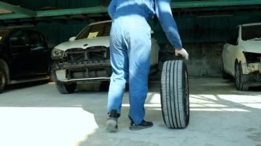 Erkek oto tamircisi ön tamponu ve diğer süspansiyon sistemlerini kaldırdı. Lastikleri sol tekere monte ediyor. Garajın içinde tamir ediliyor..