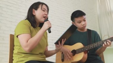 Mutlu aile birlikte müzik yapıyor: Asyalı anne ve oğul boş zamanlarını anne ve oğul arasında bağ kurmak için gitar çalarak geçiriyorlar..
