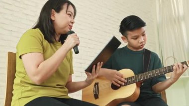 Mutlu aile birlikte müzik yapıyor: Asyalı anne ve oğul boş zamanlarını anne ve oğul arasında bağ kurmak için gitar çalarak geçiriyorlar..