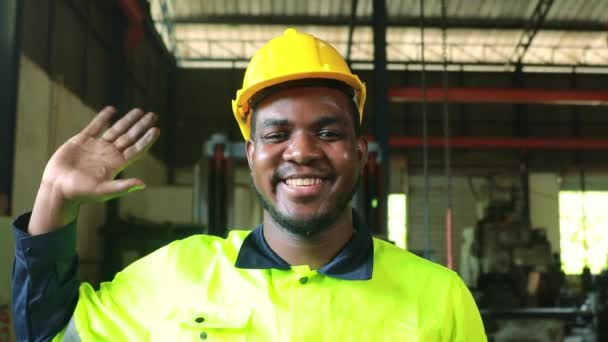 若いエンジニアの肖像 重工業で働くアフリカ系アメリカ人男性労働者 幸せなプロのヘルメットを身に着けている カメラを見てフレンドリーな幸せな労働者を迎える — ストック動画