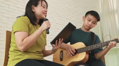 Mutlu aile birlikte müzik yapıyor: Asyalı anne ve oğul boş zamanlarını anne ve oğul arasında bağ kurmak için gitar çalarak geçiriyorlar..
