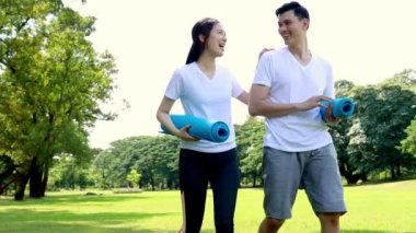 Gölgeli bahçede egzersizden sonra bahçede yoga minderleri tutan mutlu çift yürür ve birbirlerine bakarlar..