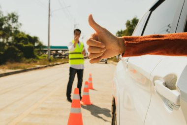 Sürücü ehliyeti ile baş parmağını gösteren genç bir kadının eli: Sürücü eğitmeninden sorumlu erkek sürücü, test sırasında arabayı güvenli bir şekilde geri viteste sürmeye hazır olduğunun sinyalini verdi..