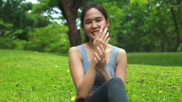 アジアの女性は心配せずに快適に座って 日焼け止めを適用し 肌を保護し 紫外線から手のひらをマッサージします 健康のための紫外線庭園の発汗熱でいくつかの運動をお楽しみください — ストック動画