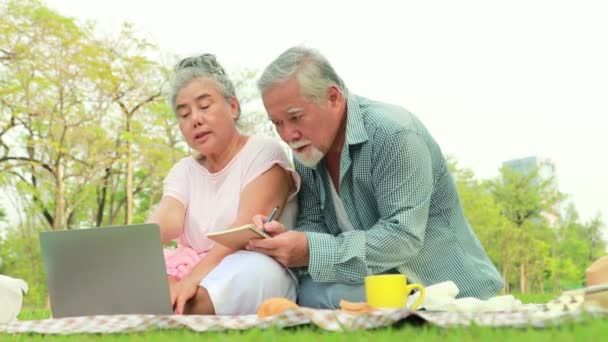 アジアの高齢者のカップルは 良い気分でタブレットからノートパソコンのノートブックに重要なメッセージ年金を詰め込む公園のリラックスに座って日陰の庭でキャンプします — ストック動画