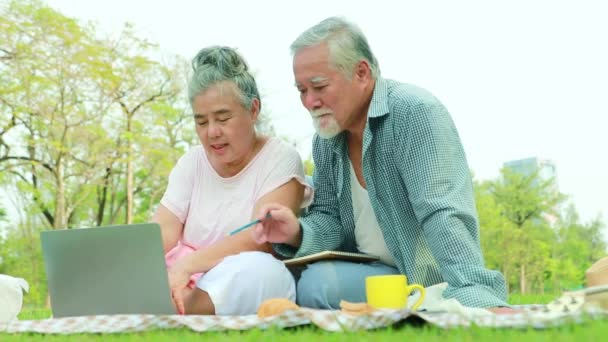 アジアの高齢者のカップルは 良い気分でタブレットからノートパソコンのノートブックに重要なメッセージ年金を詰め込む公園のリラックスに座って日陰の庭でキャンプします — ストック動画