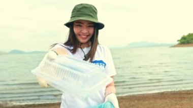 Portre gönüllüsü güzel Asyalı kadın gönüllüler plastik kutulardan çöp topluyor ve onları gönüllü ve gururla plastik torbalara koyup küresel ısınmayı azaltmak için geri dönüşüm toplumuna yardım ediyorlar..