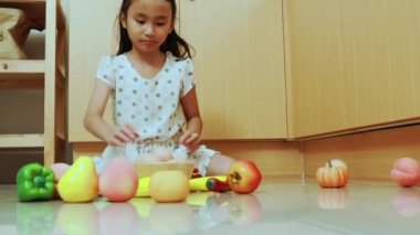 Asyalı bir kız çocuğu, renkli plastik sebze simülasyonlarıyla evde oturuyor..