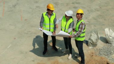 Üst düzey kadın mimar, iskelenin yanında duran ve binanın düzeltilmiş noktalarını gösteren iki erkek işçiye danıştı ve yukarıdaki ekibe aynı yolu takip etmelerini söyledi.