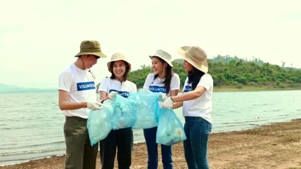 白いシャツを着たアジアのボランティアチームは 袋にペットボトルを集め ビーチをきれいにする作業チームと一緒に成功を喜びます天然水の源をきれいにする — ストック動画