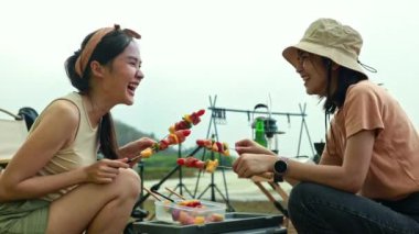 Tatil kampı aktiviteleri: İki heyecanlı Asyalı kız, gece çadırlarında uyurken lezzetli ızgara ve lezzetli barbekü yemekleri hazırlıyorlar..