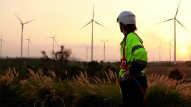 Sahada çalışan rahat erkek teknisyen mühendis, yenilenebilir enerji üretim istasyonu güneş batarken çevreye elektrik üretmek için doğal rüzgar ve rüzgar türbinleri kullanıyor..