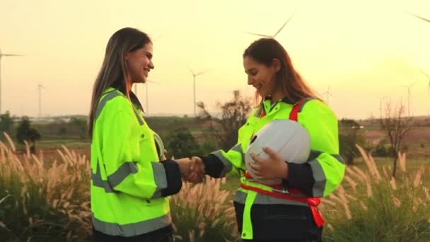 ポートレイト2人の女性技術者 優秀な同僚は仕事を終え 成功したチームワークの後の夕方に風車フィールドで手を振ります — ストック動画