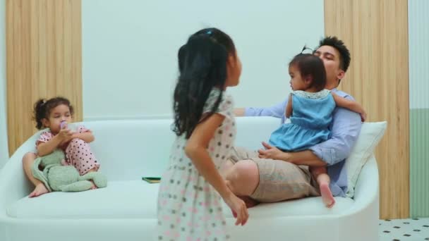 アジアの父親は彼の子供を世話し 彼の娘を抱くことは彼女のめまいを作るソファーの周りを走っている不気味な長女と頭痛を持つでしょう 彼女を叱ります — ストック動画