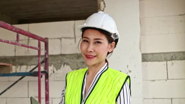 笑顔でカメラを見て肖像画の美しい女性建築家 白い安全ヘルメットを着て建設現場の建物で働くアジアの女性建築家のエンジニア — ストック動画
