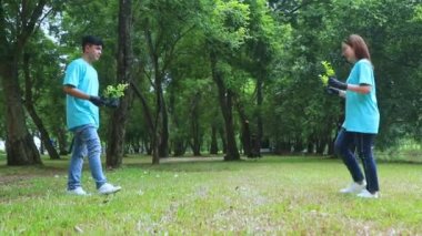 Genç Asyalı erkek ve dişi gönüllüler, yeşilliği artırmak için bahçedeki çevreyi korumak amacıyla ağaç dikmek üzere fidanlarla yürüyorlar. Bahçede birlikte büyüyelim, gururla gülelim..