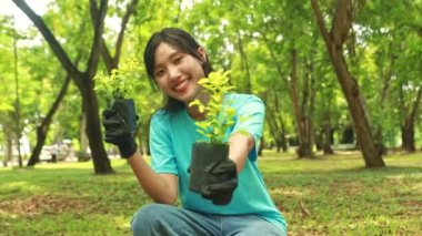 Genç, sevimli Asyalı bir kadın bahçedeki boş alanı korumak için gönüllü ağaç dikiyor. Yeşillik ekliyor. Ağacın fidanını mutlu bir gülümsemeyle kameraya bakarken gösteriyor..