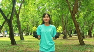 Genç, sevimli Asyalı bir kadının gönüllü olarak ağaç dikmeye gönüllü olması bahçedeki boş alanı koruması yeşillik eklemesi elinde mutlu bir gülümsemeyle kameraya bakarken ağaçların filizlenmesini gösteriyor..