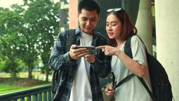 2人のアジアの大学生 男女が学校の建物内のスマートフォンでメッセージを見つめ 大学で良い気分で立って微笑んでいる — ストック動画