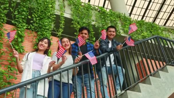 7月4日を祝う米国旗を掲げて振るハッピーグループアジアの大学生は 学校の建物のステップに沿って立っています — ストック動画