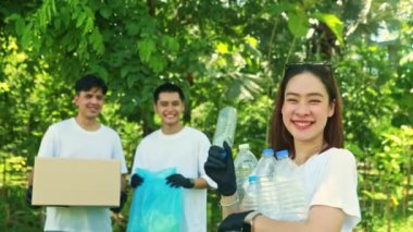 Gönüllü gençlik gönüllüleri hayır işleri cemiyetinde çalışıyor: Parktan atılan plastik şişeleri toplayıp kutuya koyan erkek arkadaşlarının önünde gülümseyen kadın gönüllüler.