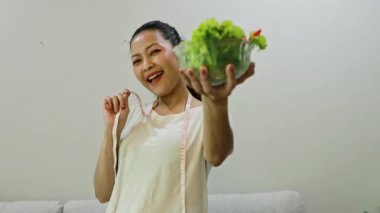 Neşeli mutlu Asyalı kadın yaşam tarzı salata yerken bir kase domates, dolma biber, taze sebze ve mezura yemek kilo vermek, zayıf ve sağlıklı kalmak istiyor..