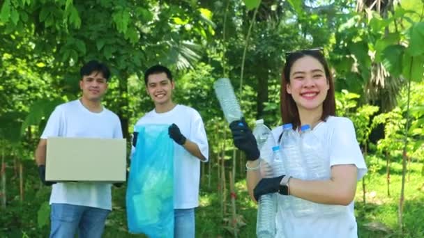 ボランティア志願の若者ボランティアが良い行いをする社会 男性の友人の前で笑顔の女性ボランティアが公園で捨てられたプラスチックボトルを拾って箱のリサイクルに置く — ストック動画