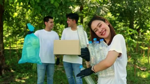 ボランティア志願の若者ボランティアが良い行いをする社会 男性の友人の前で笑顔の女性ボランティアが公園で捨てられたプラスチックボトルを拾って箱のリサイクルに置く — ストック動画