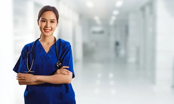 Portrait asian female surgeon healthy in blue uniform with stethoscope standing crossed hands smiling friendly looking at camera all smart stand in abstract medical facility.