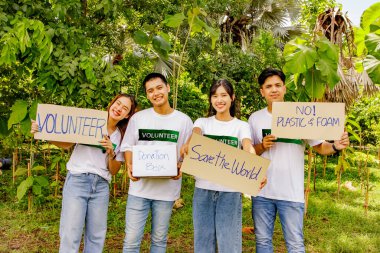 Grup Asyalı erkek ve kadın gönüllüler kağıt pankart taşıyorlar. Çevre koruma kampanyası. Etrafa çöp atma ve orman ekme faaliyetlerinde kirliliğe yol açan plastik veya köpük kullanmaktan kaçınma..