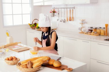 Küçük tatlı Asyalı aşçı öğrenci aşçı mutfakta lezzetli yemekler yapmayı öğreniyor. Bir yumurta kasesinde baharat ve biber hazırlayın: Aşçılık ve beslenme öğrenme okulunda konseptler.