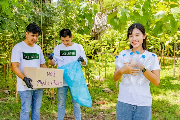 Working voluntary youth volunteers doing good deeds society : Happy smiling female volunteers in front of male friends picking up discarded plastic bottles in the park putting them in box recycle.
