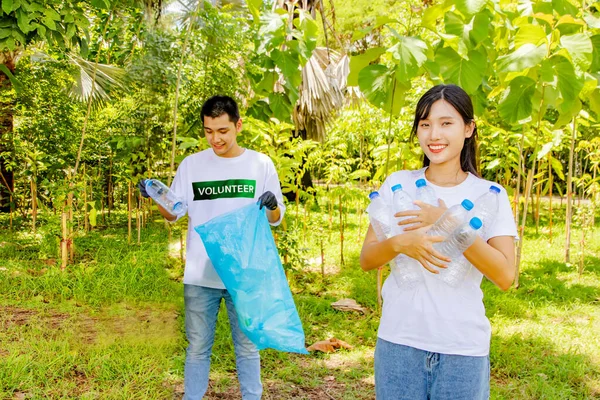 Working voluntary youth volunteers doing good deeds society : Happy smiling female volunteers in front of male friends picking up discarded plastic bottles in the park putting them in box recycle.